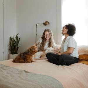 puštanje odrasle dece, nasmejane žene sede na krevetu i igraju se sa psom