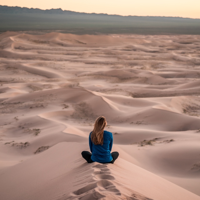 Milenijalkama koje uskoro pune 40 godina, žena sedi u pustinji, na pesku, i gleda u daljinu
